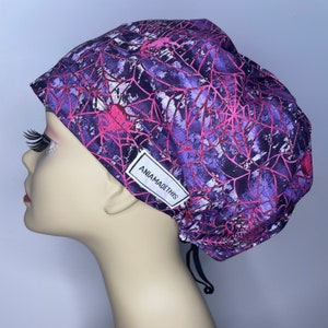 May include: Purple and pink patterned surgical scrub hat with a black drawstring and a white label that reads "AniamAdeThis".