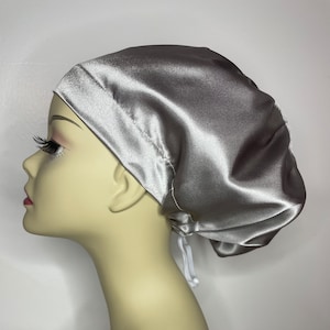 May include: A silver satin sleep cap with a white drawstring. The cap is designed to protect hair while sleeping.