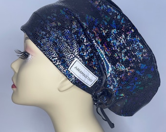May include: Black surgical scrub hat with a iridescent, textured, snake skin pattern. The hat has a drawstring and a white label that reads "ANIAMADETHIS".