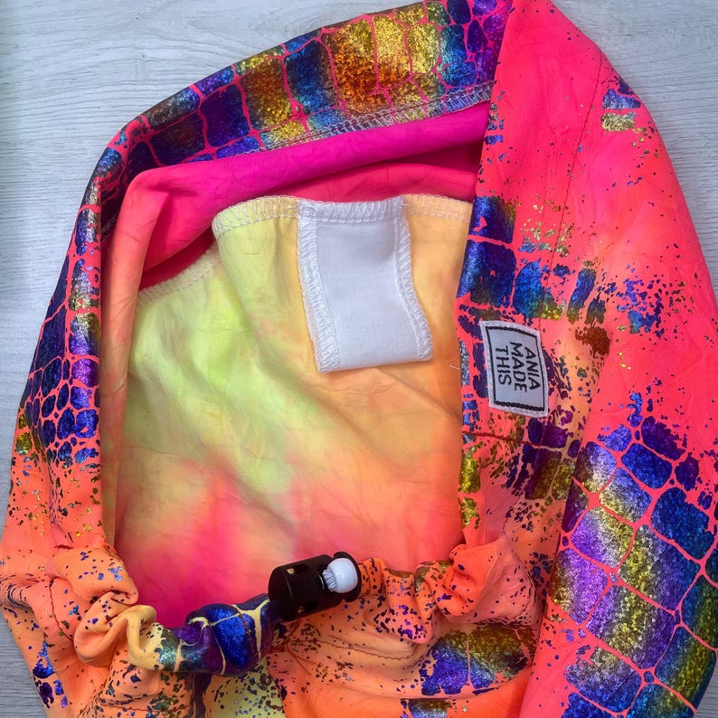 May include: A pink, yellow, and blue tie-dye fabric with a white label that says "ANIA MADE THIS". The fabric has a holographic, iridescent, and scaly pattern.