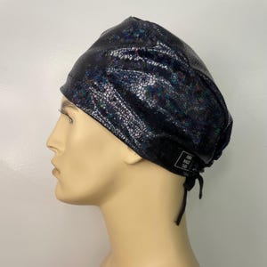 May include: Black scrub hat with a iridescent snakeskin pattern. The hat has a black tie and a label that reads "Anna Made This".