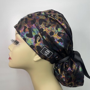 May include: A black scrub hat with a leopard print and iridescent finish. The hat has a tie at the back and a small black label that says "ANIA MADE THIS".