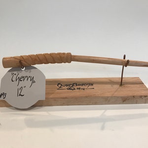 以下が含まれることがあります： ねじれたデザインのチェリーウッド製の30.5cmのウッドワンド。ワンドは、金属製のワイヤーホルダーが付いた木製スタンドに飾られています。スタンドのラベルには、「チェリー」と「12」と「GoryBeams Wood Shop」と書いてあります。