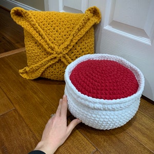 May include: A crocheted mustard yellow cushion and a crocheted white and red storage basket. The basket has a red interior and a white exterior.