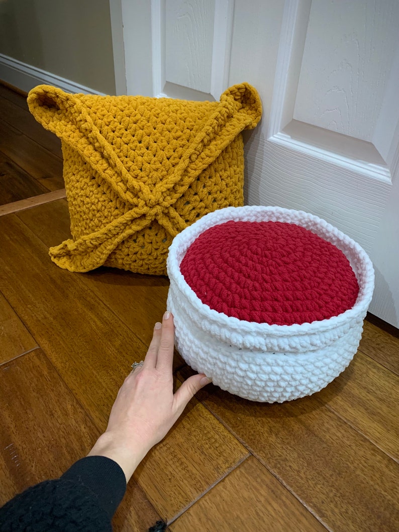 May include: A crocheted mustard yellow cushion and a crocheted white and red storage basket. The basket has a red interior and a white exterior.