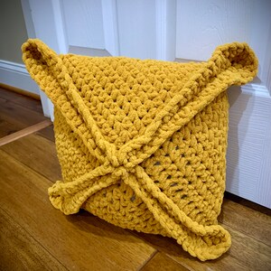 May include: A mustard yellow crocheted cushion with a unique, geometric design. The cushion is made with a soft, fluffy yarn and has a slightly textured surface.