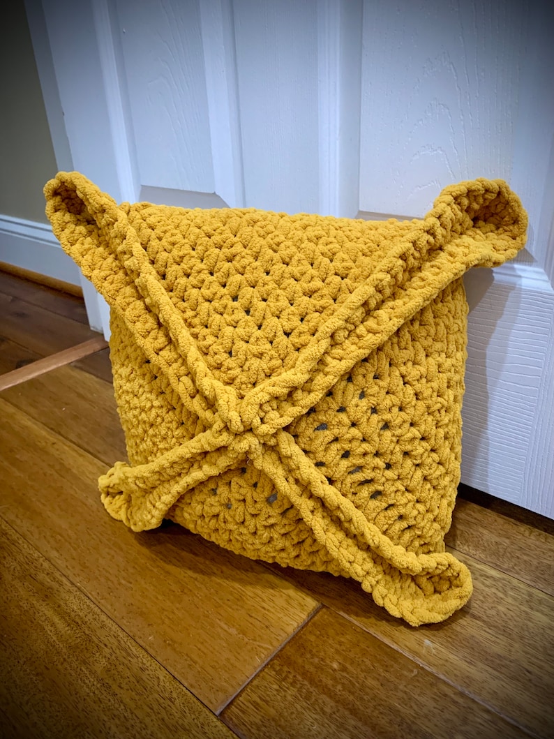 May include: A mustard yellow crocheted cushion with a unique, geometric design. The cushion is made with a soft, fluffy yarn and has a slightly textured surface.
