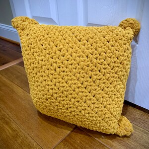 May include: A mustard yellow crocheted cushion with pom-poms on the corners.