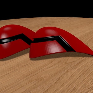 Pode incluir: Dois objetos de plástico vermelho com forma de capacete com detalhes pretos. Os objetos estão sobre uma superfície de madeira.