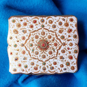 May include: A white, ornate, decorative box with a gold and jewel-toned design. The box is decorated with a floral pattern and has a raised centre with a jewel-toned design.