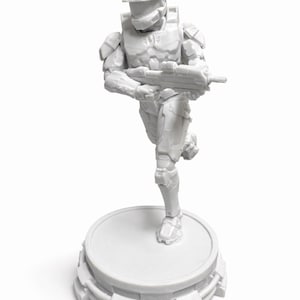 Puede incluir: Figura blanca de un soldado futurista en pose de carrera, sosteniendo un rifle. La figura está sobre una base circular con un diseño detallado y en capas. La estética general es limpia y moderna.