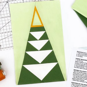 Op de afbeelding: Een groene, witte en gele stoffen kerstboom quiltblok met instructies voor het naaien van het blok. De instructies omvatten een lijst met stoffenvereisten, aanwijzingen voor het naaien en hoe je de secties naait.