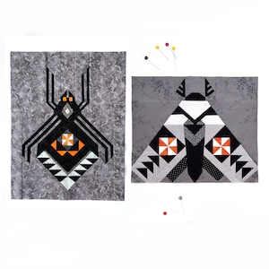 May include: Two fabric quilt blocks featuring a spider and a moth design. The spider block has a gray floral background with black, white, and orange geometric accents. The moth block features gray, black, white, and orange patterns with sewing pins.
