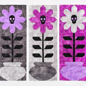 May include: Three fabric panels feature stylized flowers with skull centers. The flowers are in shades of purple, white, and gray, with black stems and leaves. Each flower sits in a gray vase, creating a unique gothic floral design.