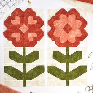 Può includere: Due blocchi di fiori in tessuto. Ogni blocco presenta un fiore rosso con un design a petali a forma di cuore, stelo verde e foglie. Lo sfondo è di colore crema chiaro. I blocchi fanno probabilmente parte di un progetto di quilting.