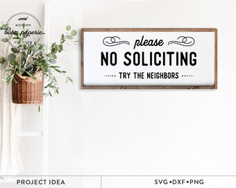 May include: A white sign with a brown wood frame that reads "please NO SOLICITING - TRY THE NEIGHBORS -" in black text. The sign is hanging on a white wall.