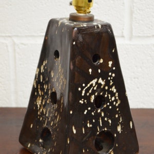 May include: A brown ceramic table lamp with a white speckled glaze. The lamp has a square base and a pyramid-shaped shade with holes. The lamp has a brass socket.