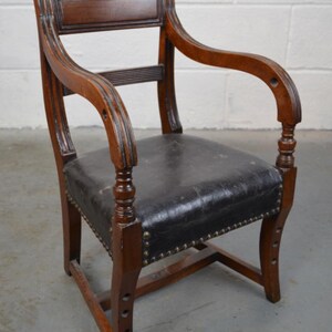 May include: A dark brown wooden armchair with a black leather seat. The chair has a curved back and arms, and the seat is studded with brass tacks.