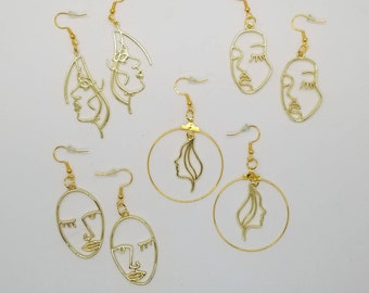 May include: Set of gold-toned earrings featuring abstract face designs. Some earrings are hoop style with a face design inside the hoop. Other earrings are dangle style with a face design on the dangle.
