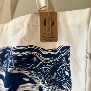 Puede incluir: Una bolsa de lona blanca con orcas y olas impresas en azul y blanco. La bolsa tiene una etiqueta de papel marr&oacute;n con la palabra "Redivvus" impresa en ella.