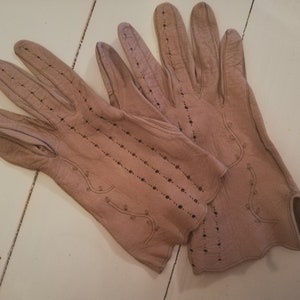 Puede incluir: Un par de guantes de cuero marrón claro con costuras delicadas y un diseño perforado.