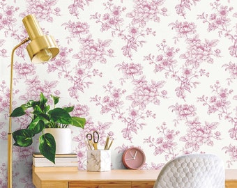 May include: A home office with a white desk and a white chair. The wall is covered in pink floral wallpaper. There is a lamp, a plant, and a clock on the desk.