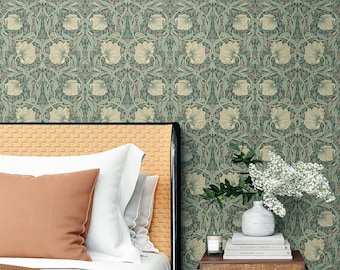 Könnte beinhalten: Ein Schlafzimmer-Interieur mit einem Bett mit einer braunen Decke und weißen Kissen. Ein Nachttisch mit einer Schublade und einem unteren Regal steht neben dem Bett. Auf dem Nachttisch stehen eine weiße Vase mit weißen Blumen, eine Kerze und Bücher. Die Wand hinter dem Bett ist mit einer grünen Blumen-Tapete mit einem sich wiederholenden Muster bedeckt.