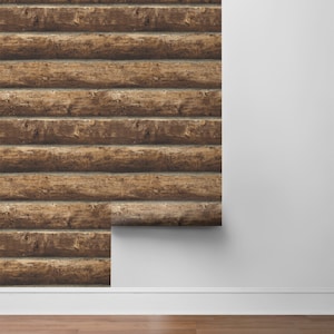May include: A roll of brown wood-look wallpaper with a rustic log cabin design. The wallpaper is partially unrolled and is being applied to a white wall.