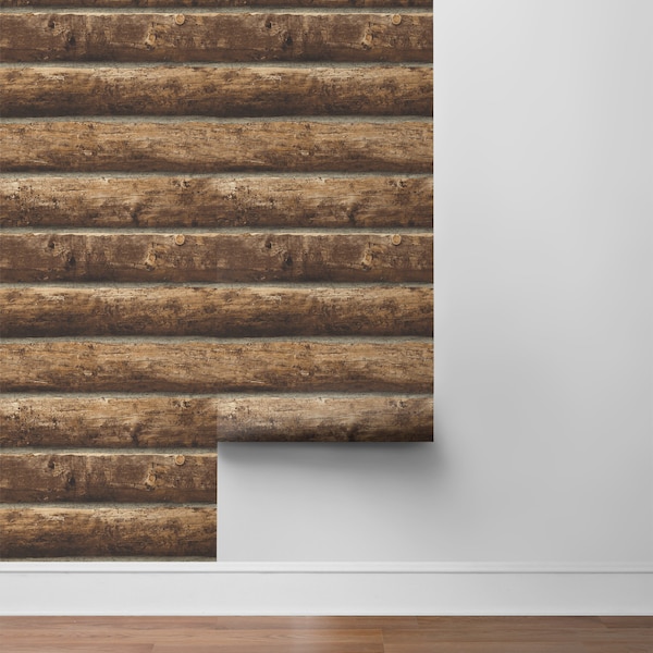 May include: A roll of brown wood-look wallpaper with a rustic log cabin design. The wallpaper is partially unrolled and is being applied to a white wall.