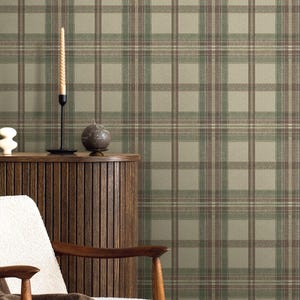 May include: A room scene featuring a plaid wallpaper in shades of green, brown, and beige. A wooden cabinet, a white chair with wooden arms, and a brown blanket are in the foreground. A tall, twisted candle sits on a black candle holder.