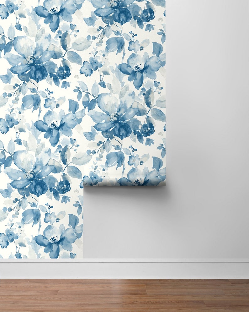 May include: A roll of blue and white floral wallpaper with a watercolor design. The wallpaper is being unrolled on a white wall.