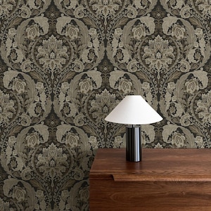 May include: A dark floral wallpaper with a repeating pattern of stylized flowers and leaves in shades of brown and beige. A modern black and white table lamp sits on a wooden dresser.