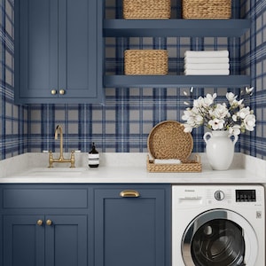 May include: A laundry room with navy blue cabinets, a white countertop, and a washing machine. Woven baskets sit on shelves against a blue plaid wallpaper. A white vase holds white flowers, and a gold faucet is visible.