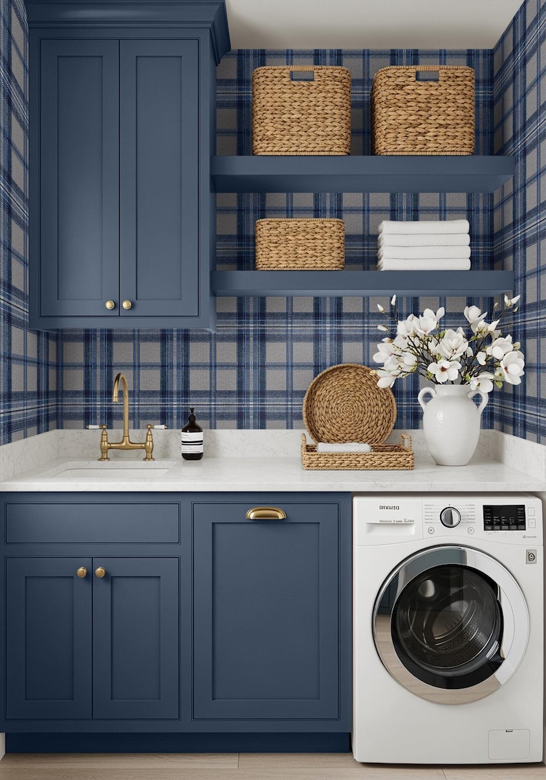 May include: A laundry room with navy blue cabinets, a white countertop, and a washing machine. Woven baskets sit on shelves against a blue plaid wallpaper. A white vase holds white flowers, and a gold faucet is visible.