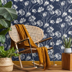May include: A rocking chair with a woven rattan seat and back, a brown throw blanket draped over the seat, and a blue floral wallpaper with white flowers in the background.