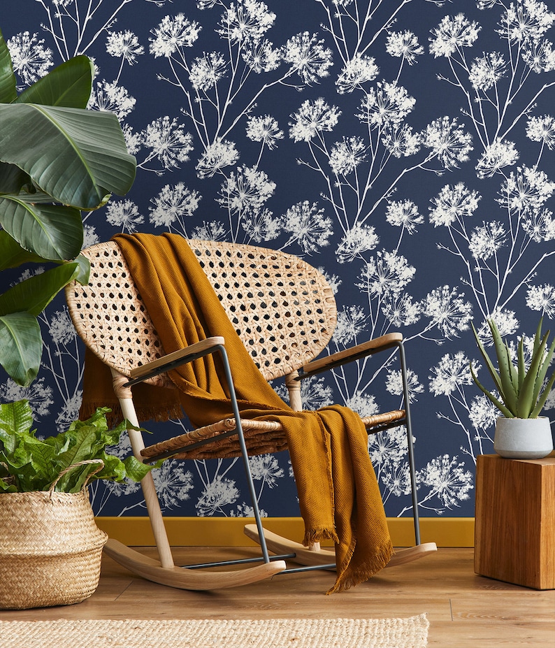 May include: A rocking chair with a woven rattan seat and back, a brown throw blanket draped over the seat, and a blue floral wallpaper with white flowers in the background.