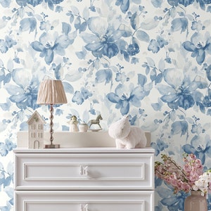 May include: White dresser with three drawers and butterfly-shaped knobs. The dresser is in front of a wall with a blue floral wallpaper pattern.