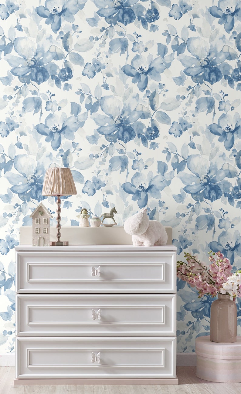 May include: White dresser with three drawers and butterfly-shaped knobs. The dresser is in front of a wall with a blue floral wallpaper pattern.