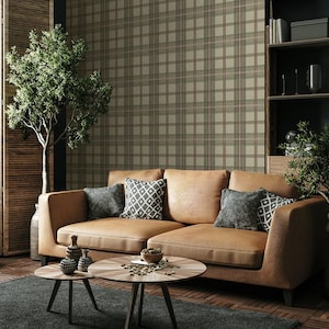 May include: A modern living room featuring a tan leather sectional sofa with decorative pillows. Two round wooden coffee tables sit on a dark gray rug. The background includes a plaid wallpaper and a small tree.
