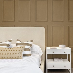 May include: A white bed with a white headboard and a white duvet cover. There are three pillows on the bed, two striped pillows and one square patterned pillow. A white nightstand with two drawers and a shelf is next to the bed. The nightstand has a small bowl on top and a book on the shelf. The wall behind the bed is covered in a brown wood panel wallpaper.