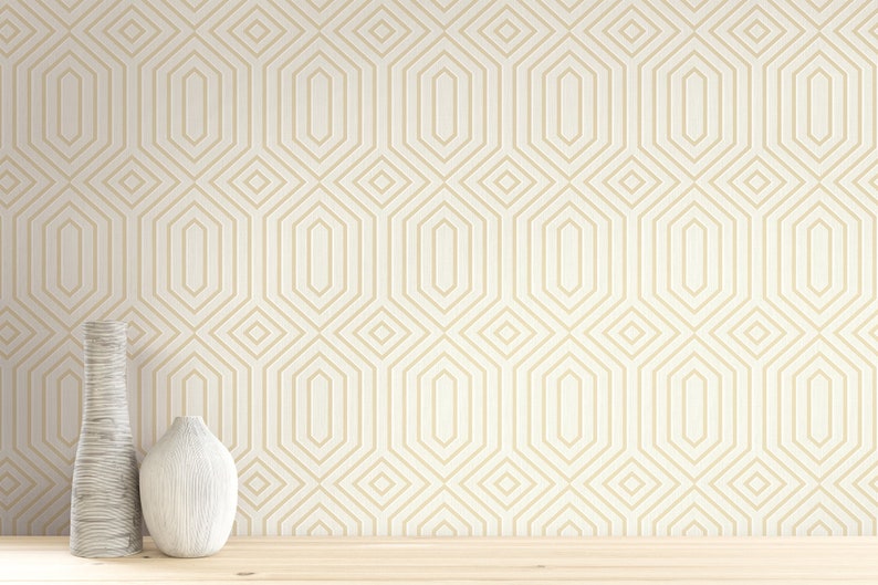 May include: A white wall with a geometric pattern wallpaper in gold. Two vases, one white and one brown, are placed on a wooden surface in front of the wall.