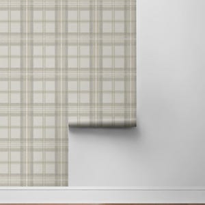 May include: A roll of wallpaper with a neutral plaid pattern in shades of beige, tan, and white. The wallpaper is partially unrolled, revealing the pattern against a white wall and hardwood floor.