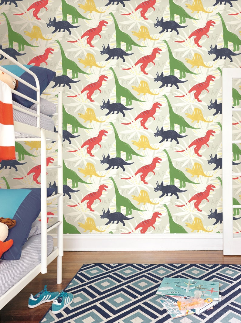 May include: A white bunk bed with a red and white striped blanket and a blue pillow. The wall behind the bed is covered in a wallpaper with a repeating pattern of green, red, yellow, and blue dinosaurs.