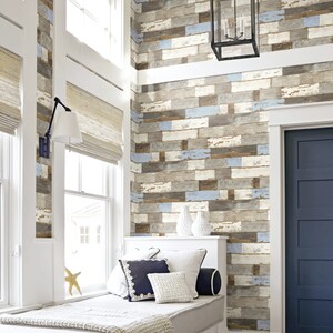 May include: A white window seat with a light brown blanket and blue and white pillows in front of a wall with a wood plank wallpaper design. A black door is on the right side of the image.