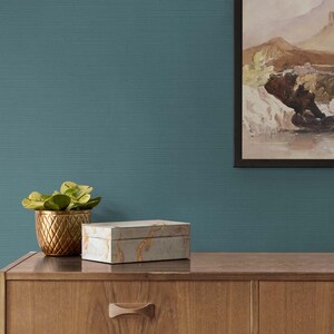 May include: A teal blue textured wall with a framed landscape painting, a small potted plant, and a decorative box on a wooden dresser.