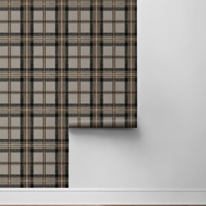 May include: A roll of wallpaper featuring a classic plaid pattern in shades of gray, black, and brown. The wallpaper is partially unrolled, revealing the pattern against a white wall and wooden floor.
