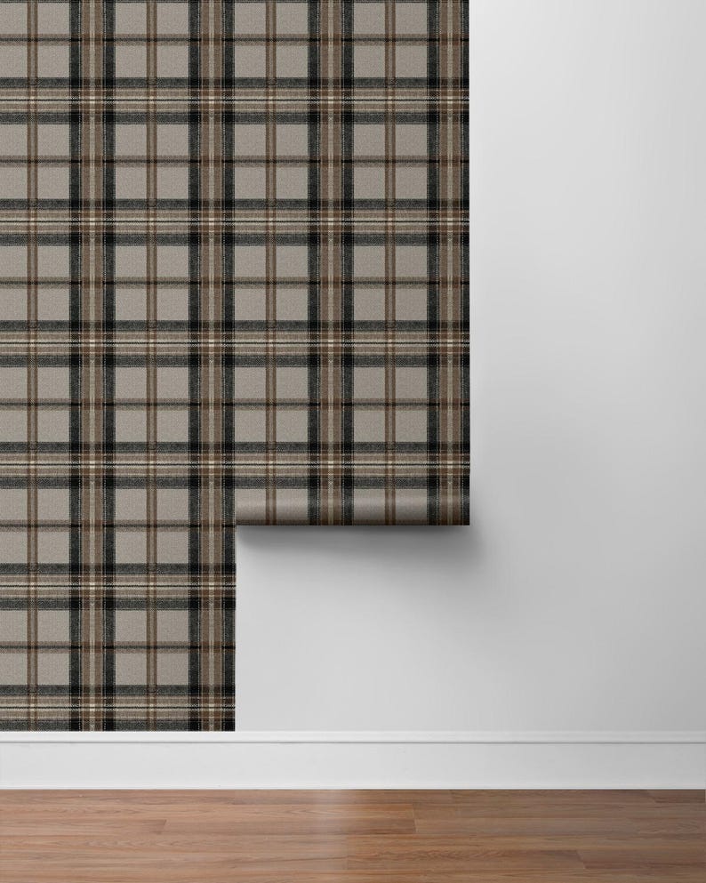 May include: A roll of wallpaper featuring a classic plaid pattern in shades of gray, black, and brown. The wallpaper is partially unrolled, revealing the pattern against a white wall and wooden floor.