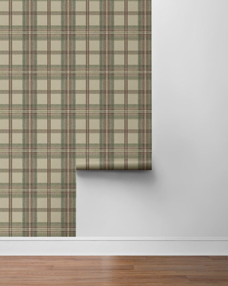May include: A roll of wallpaper with a classic plaid pattern in shades of beige, brown, and green. The wallpaper is displayed against a white wall and a wooden floor, showcasing its design and texture.