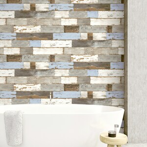 May include: A white bathtub with a white towel hanging on the side, sitting in front of a wall with a wood plank pattern in shades of brown, gray, and blue. A small wooden stool with a round top sits in the foreground.