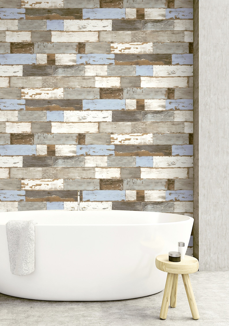 May include: A white bathtub with a white towel hanging on the side, sitting in front of a wall with a wood plank pattern in shades of brown, gray, and blue. A small wooden stool with a round top sits in the foreground.